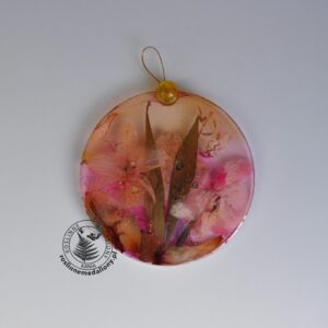 Ręcznie wykonany, okrągły medalion z żywicy, w którym zatopiono różnobarwne suszone rośliny, umieszczony na kartce papieru.