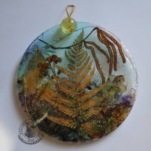 Ręcznie wykonany, okrągły medalion z żywicy, w którym zatopiono różnobarwne suszone rośliny, umieszczony na kartce papieru.