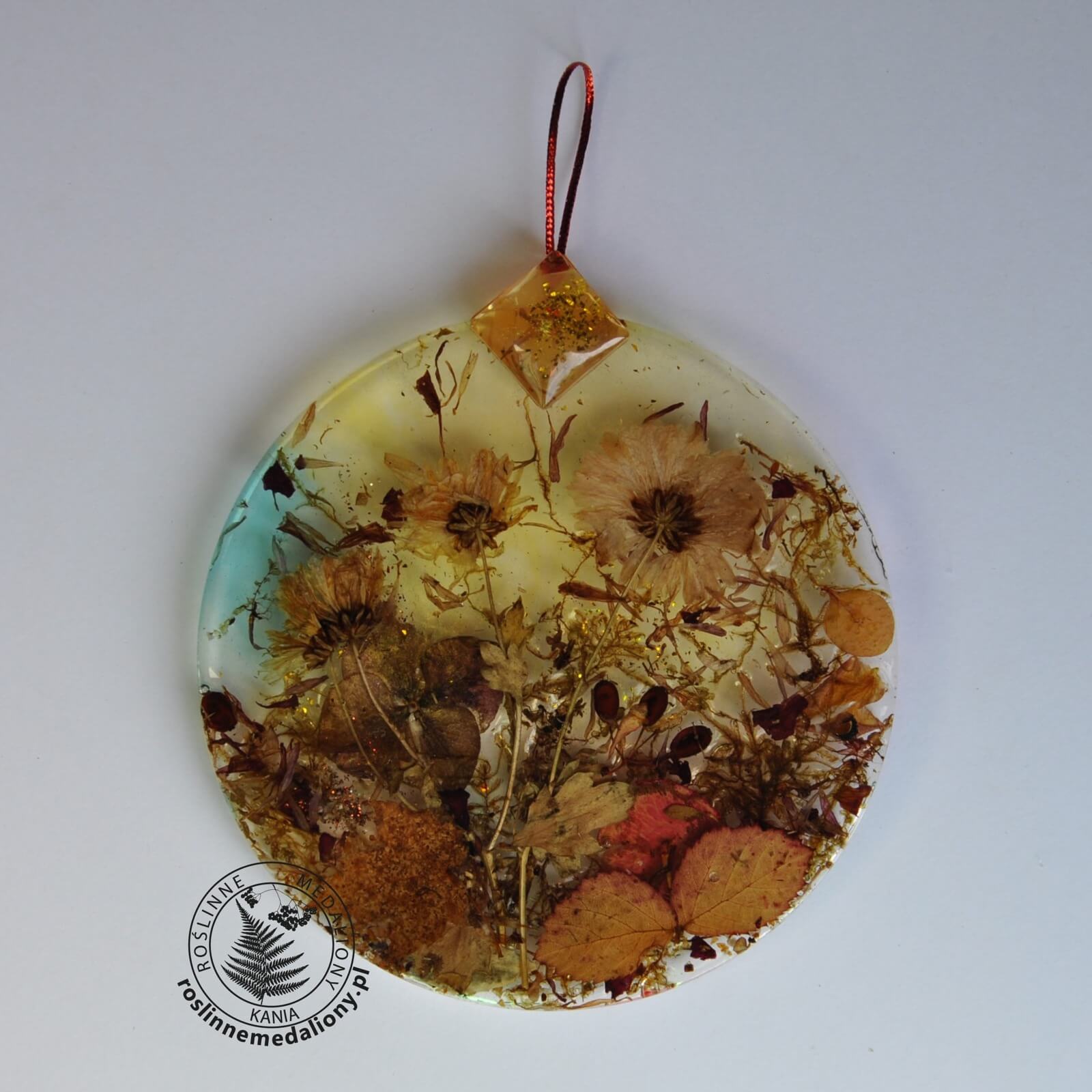 Ręcznie wykonany, okrągły medalion z żywicy, w którym zatopiono różnobarwne suszone rośliny, umieszczony na kartce papieru.